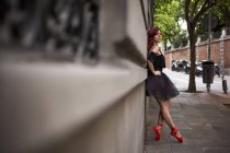 Ballerine à tête rouge avec tutu noir et pointes de ballet rouge se réchauffant pour danser dans la rue, posant, estampillée sur le mur — Photo de stock