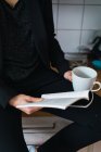 Крупный план женщины, читающей книгу, сидящей на кухонном столе с кофе — стоковое фото