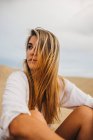Молода вдумлива блондинка сидить на піску на заході сонця — стокове фото