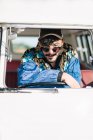 Attraente giovane uomo in abito elegante appoggiato al volante e guardando la fotocamera mentre seduto all'interno del furgone d'epoca durante il viaggio nella natura — Foto stock