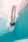 Хлопчик у стовбурах плаває в прозорому бірюзовому глибокому басейні, піднімаючи повітряні бульбашки — стокове фото