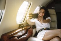 Femme gaie prenant selfie dans l'avion — Photo de stock