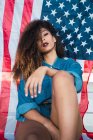 Молодая женщина в джинсовой одежде сидит перед флагом Америки — стоковое фото