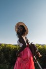Модная афроамериканка в шляпе с чемоданом и прогулкой по сельской дороге летом — стоковое фото