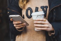 Unrecognizable woman holding smartphone and paper cup on blurred street — Stock Photo