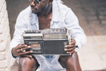 Jeune homme assis avec dispositif de radio vintage et regardant loin — Photo de stock