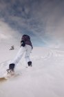 Unrecognizable female wearing warm clothes and snowboard with special ammunition gliding downhill? on cloudy sky background — Stock Photo
