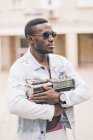 Thoughtful black man in sunglasses holding vintage radio device — Stock Photo