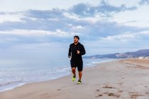 Man in sportswear running on sand at sea during outdoor workout on beach at sunset — Stock Photo