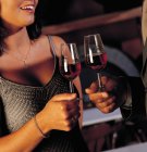 Вид на молоду жінку в одязі і чоловіка в костюмі, що стоїть в кімнаті і п'є червоне вино з окулярів — стокове фото
