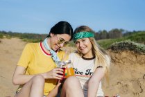Trendy girls with drinks on beach — Stock Photo