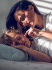 Schöne Frau liegt auf Bett hinter süßem Jungen und berührt seine Wange vorsichtig — Stockfoto