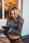 Jeune femme blonde excitée en haut scintillant tenant la caméra — Photo de stock