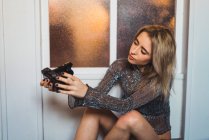 Young blonde woman in glittering top sitting on floor and holding camera — Stock Photo