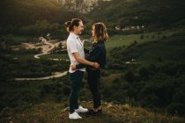 Linda pareja abrazándose mientras está de pie en el fondo del hermoso valle y las montañas - foto de stock