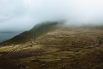 Crooked rural road in green mountains in clouds on Feroe Islands — Stock Photo