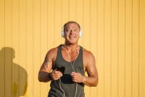 Homem mais velho forte posa com fones de ouvido no fundo amarelo — Fotografia de Stock