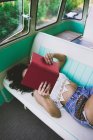 Woman lying inside retro caravan and reading book — Stock Photo
