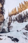 Rio que corre no lago montanhoso derretido na fenda nevada com rochas marrons e poucos abetos de inverno no dia ensolarado — Fotografia de Stock