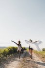Fröhlich gestylte multiethnische Frauen mit Koffer und Schal laufen aufgeregt durch sommergrüne Landschaft — Stockfoto