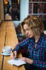 Frau sitzt im Café und schreibt in Notizbuch — Stockfoto