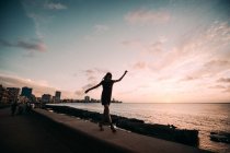 LA HABANA, CUBA - MAY 1, 2018: Romantic playful girl walking in balance on fence of concrete waterfront with city of Cuba and ocean on background. — Stock Photo