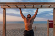 Barbudo hombre sin camisa escalando escalera de madera mientras hace ejercicio en la playa - foto de stock