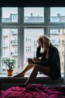 Romantique jeune femme blonde assise sur le rebord de la fenêtre avec une tasse de café — Photo de stock