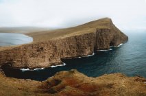 Ocean and rocky cliff under cloudy sky on Feroe Islands — Stock Photo