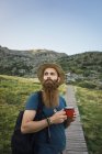 Молодий чоловік стоїть на шляху в горах з чашкою і дивиться геть — стокове фото