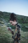 Junge lachende Frau in gemustertem, stylischem Kleid steht in der Nähe eines grünen Hügels — Stockfoto