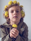 Boy with flowers in hair making faces on grey background — Stock Photo