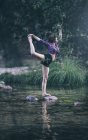 Red haired girl performs exercises by the river — Stock Photo