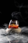 Состав стекла в миске наполнен красным пряным алкогольным коктейлем и подается на стол в дыму на черном фоне — стоковое фото