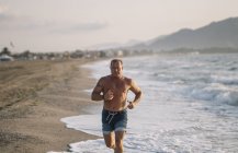 Le vieil homme fort fait de l'exercice sur la plage — Photo de stock