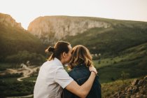 Couple mignon embrassant et endurcissant les fronts tout en étant assis sur une pente rocheuse sur fond de belle vallée et de montagnes — Photo de stock