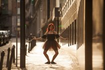 Ballerina rossa con tutù nero e punte di balletto rosso che balla per strada con sfondo retroilluminato al tramonto — Foto stock