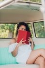 Porträt einer Frau, die im Retro-Wohnwagen sitzt und Buch in der Hand hält — Stockfoto