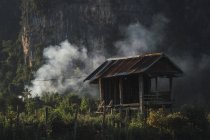 Pequena cabana de madeira e fumaça na natureza — Fotografia de Stock