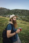 Молодий чоловік стоїть на шляху в горах з чашкою і дивиться геть — стокове фото
