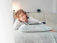 Продуманий хлопчик лежачими Цифрова табличка на дивані і дивитися вбік — стокове фото