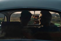 Rückansicht von zwei nicht wiedererkennbaren jungen Männern, die sich umarmen und die Natur bewundern, während sie im Retro-Auto sitzen — Stockfoto