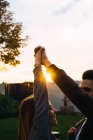Jovens pessoas alegres de mãos erguidas enquanto olham um para o outro sob a luz do pôr do sol. — Fotografia de Stock