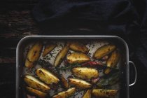 Roasted golden crunchy potato wedges in baking pan on wooden table — Stock Photo