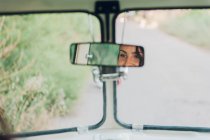 Riflessione della giovane donna nello specchio retrovisore di auto retrò durante il viaggio nella natura — Foto stock
