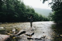 Pescatore che tiene la canna da spinning e in piedi sulle rocce sul flusso del fiume — Foto stock