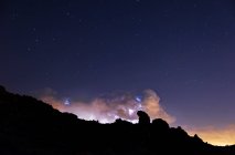 Rays and clouds in night storm over the mountain under a starry sky - foto de stock
