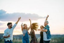 Grupo de jovens em trajes casuais rindo e dançando enquanto se divertindo na bela paisagem juntos — Fotografia de Stock