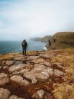 Uomo escursionista irriconoscibile in piedi sulla costa con bastone e guardando l'oceano sulle isole Feroe — Foto stock