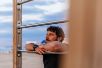 Thoughtful bearded man in sportswear leaning on ladder and looking away while resting during outdoor training — Stock Photo